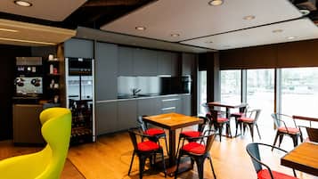 A modern kitchen with built-in appliances, a dining area with wooden tables and red chairs, and large windows offering a view.
