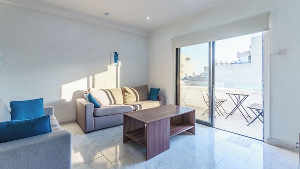 A modern living room with a sofa, coffee table, and a balcony with outdoor furniture. - Fanta Sea Apartment (Larnaca)
