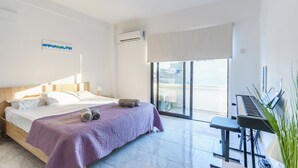 A modern hotel room with a bed, a piano, and a view of the city through large windows. - Fanta Sea Apartment (Larnaca)