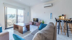 A modern living room with a sofa, a wooden coffee table, a TV, and a dining area with a table and chairs. - Fanta Sea Apartment (Larnaca)