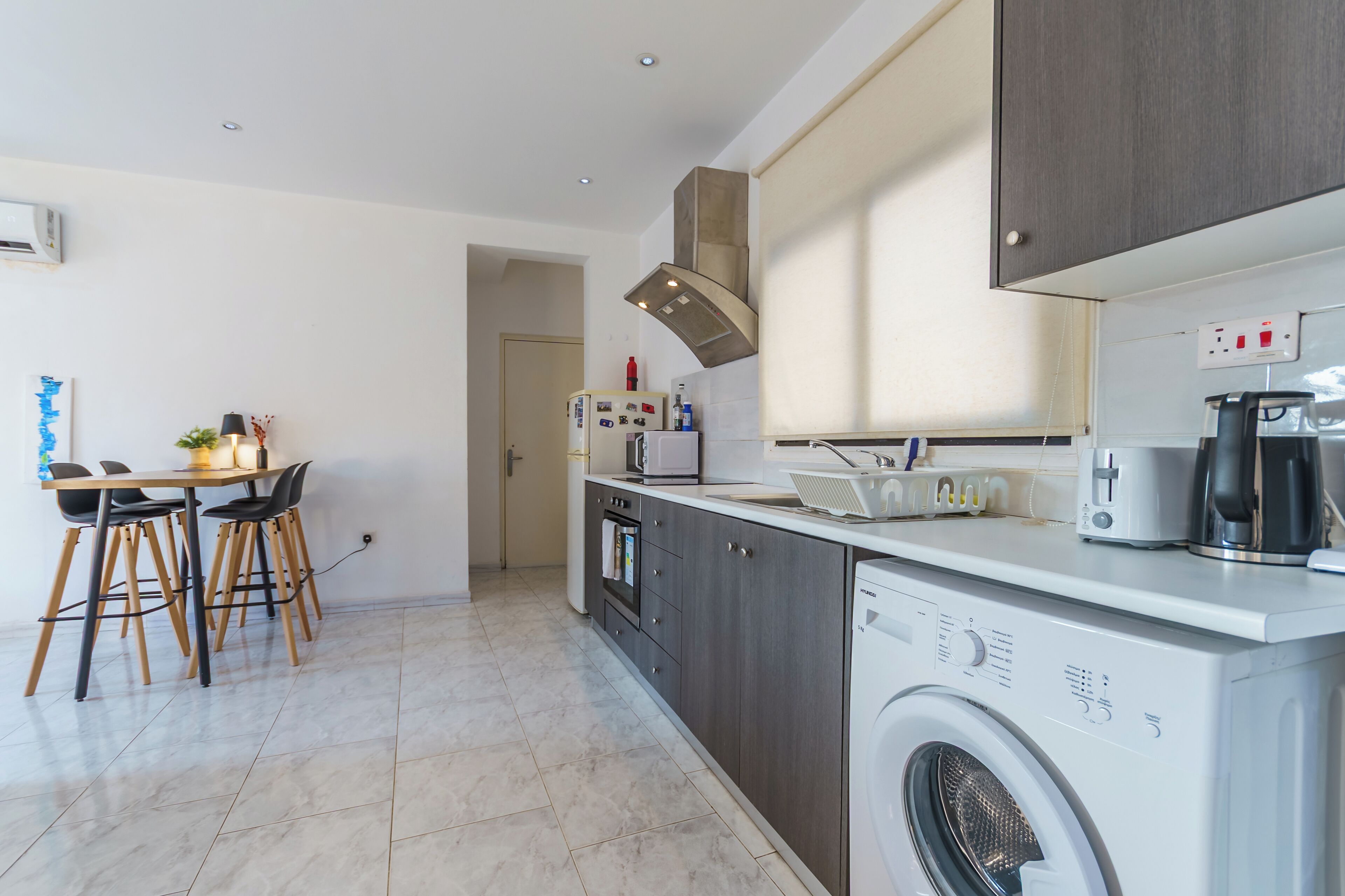 A modern kitchen with a built-in washing machine, a dining area with stools, and a microwave.