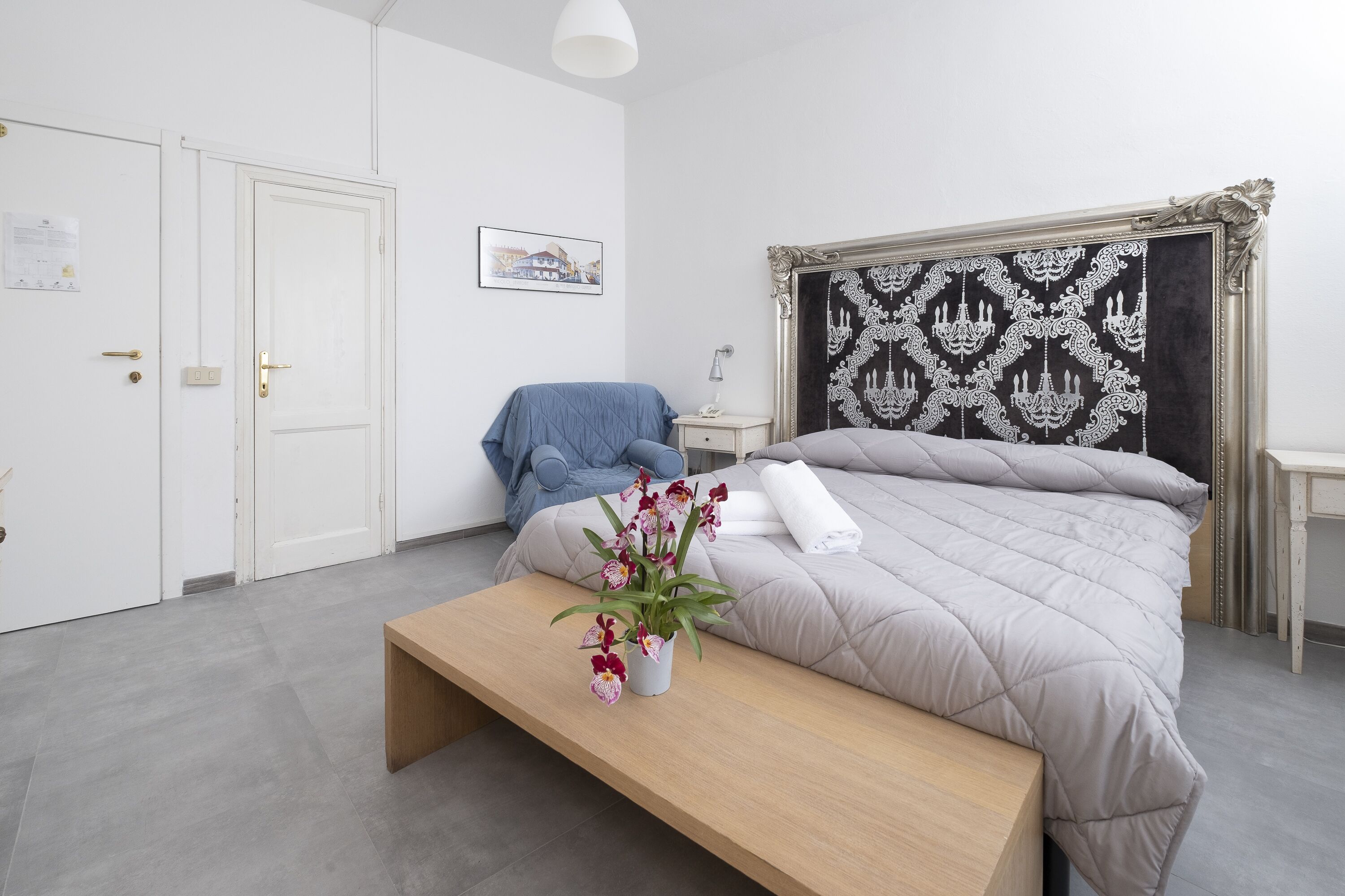 A modern bedroom with a bed, a bench, a chair, a bedside table, and a wall-mounted lamp.