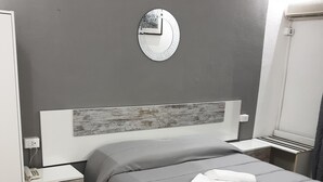 A modern bedroom with a grey bed, a wooden headboard, a bedside table with a phone, and a wall clock. - Historic Seafront Villa, 10 meters from the sea on the Tyrrhenian coast (Rosignano Solvay-Castiglioncello)
