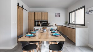 A modern kitchen with wooden cabinets, a central island, and a dining area with black chairs and a wooden table.
