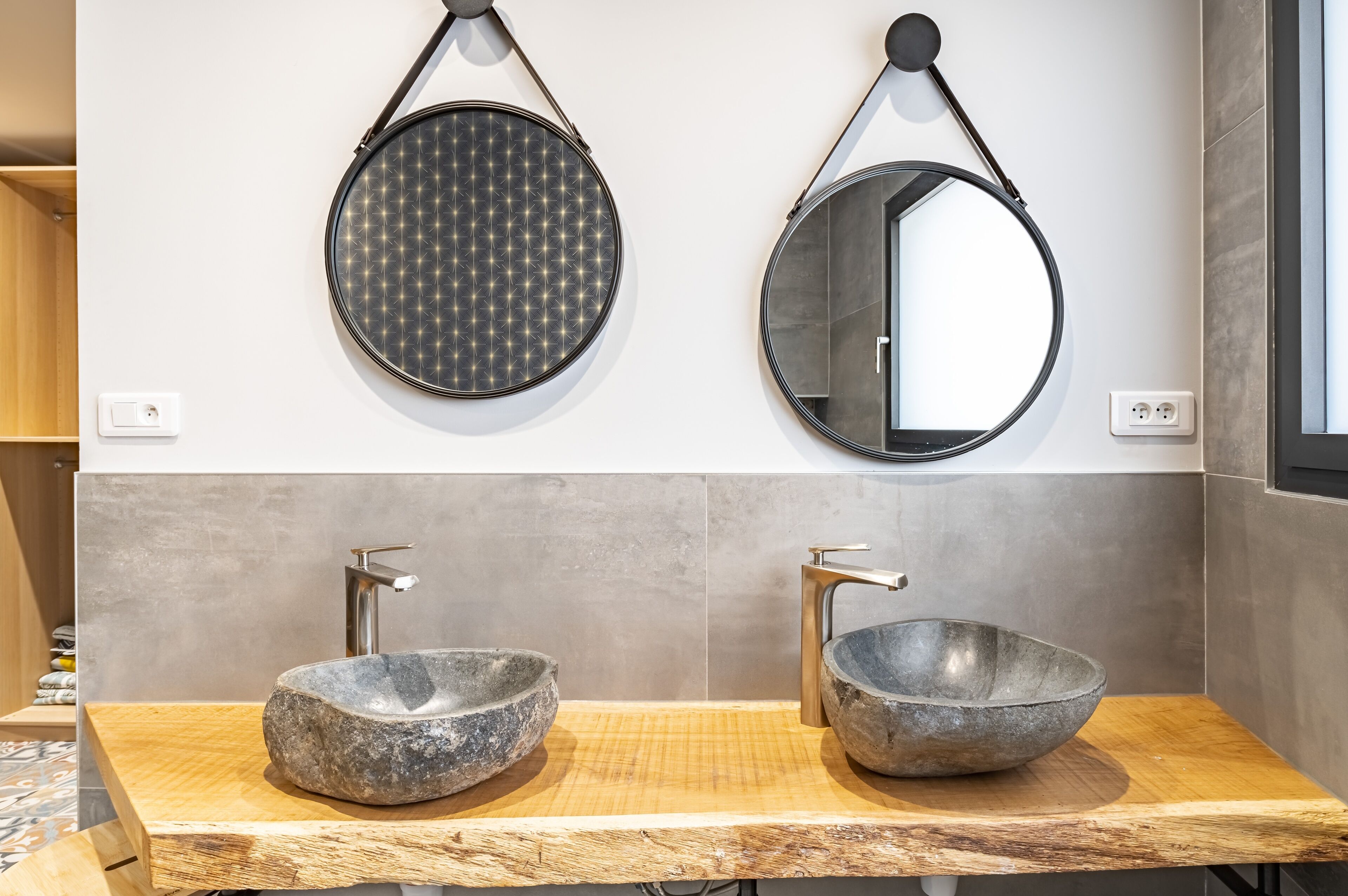 A bathroom with two round mirrors, a wooden vanity, and a stone sink.
