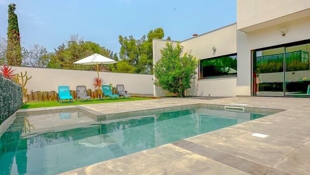 A modern outdoor pool area with a clear blue pool, surrounded by a paved patio.