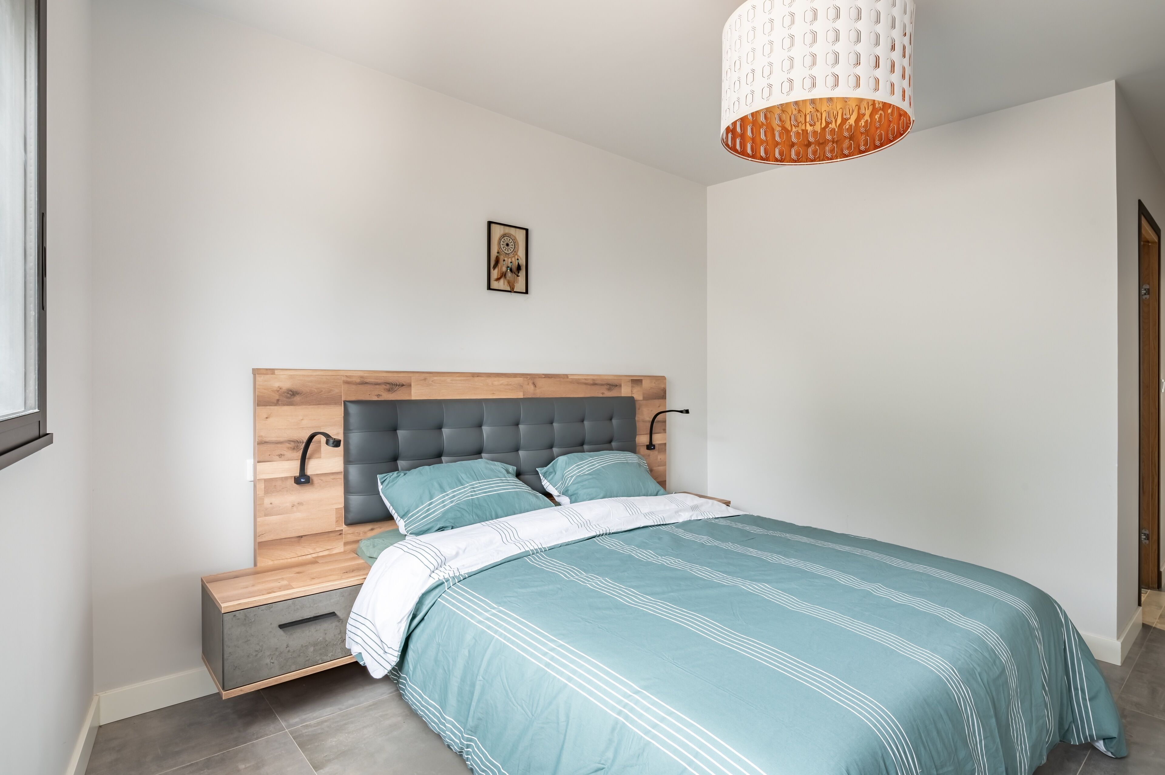 Et soveværelse med seng, natbord og vægmonteret lampe.
