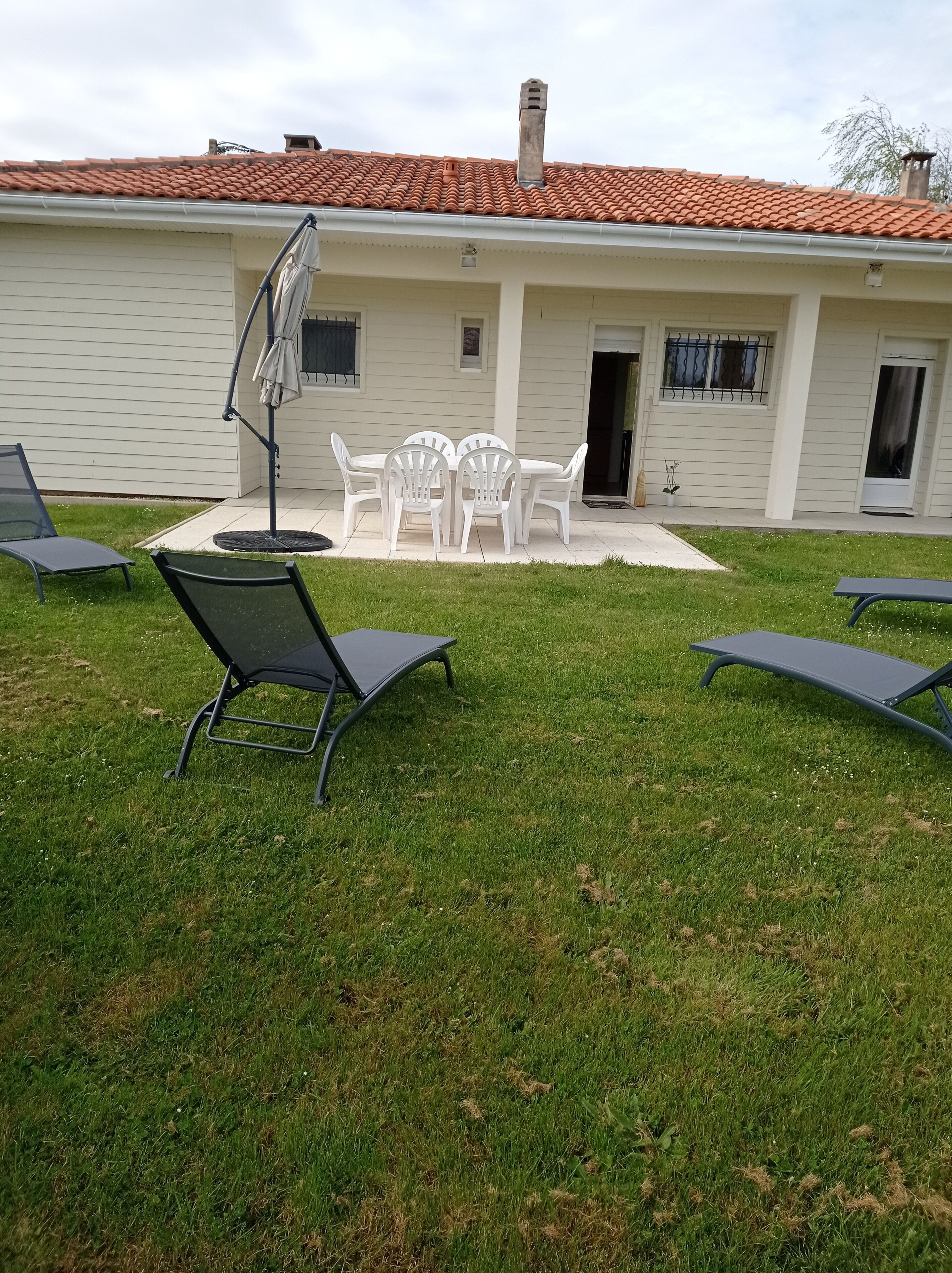 Un patio con mesa y sillas, una sombrilla y sillones de descanso.