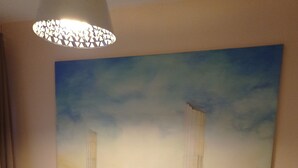 A bedroom with a large bed, striped bedding, a nightstand with a lamp, and a large painting of a beach scene on the wall.