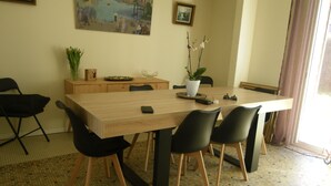 A dining area with a wooden table, black chairs, a potted plant, and a painting on the wall.