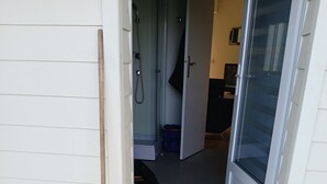 A door with a broom leaning against the wall, a shower area visible through the glass door, and a black and white patterned mat at the entrance.