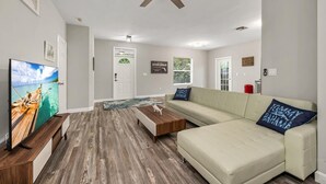 Una sala de estar con piso de madera, un sofá, una mesa de centro, un televisor y un ventilador de techo.