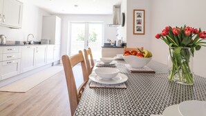 A modern kitchen with white cabinets, a dining table with a patterned tablecloth, and a vase with red flowers. - Ty Owen (Bangor)