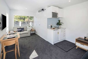 A compact living space with a kitchenette, a dining area, and a seating area with a view of greenery outside.