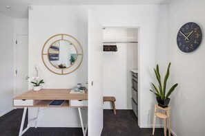 Une chambre moderne avec un bureau en bois, un miroir rond, une horloge, une plante en pot et une armoire.