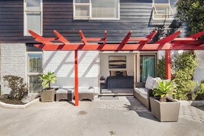 Une maison moderne dotée d’un espace extérieur aménagé et abrité, d’une chambre visible de l’extérieur et de plantes en pot.