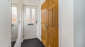A hallway with a white door, a wooden door, and a glass door with a metal handle.