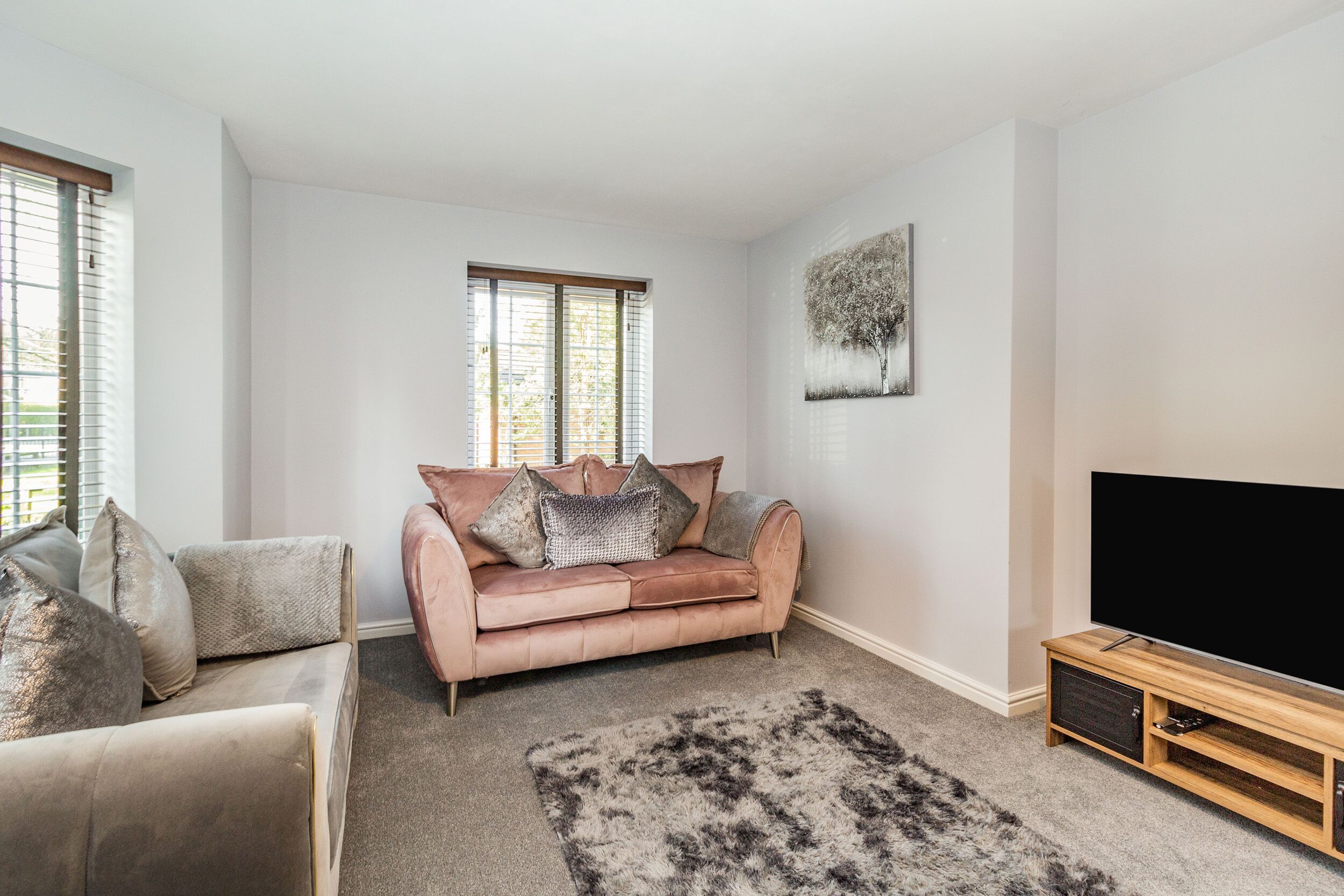 Una sala de estar con un sofá color beige, un sofá rosa, un televisor plano grande y un mueble de entretenimiento de madera.