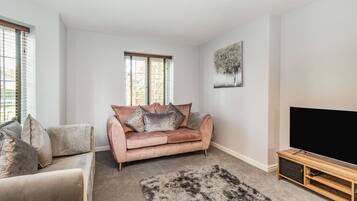Una sala de estar con un sofá color beige, un sofá rosa, un televisor plano grande y un mueble de entretenimiento de madera.
