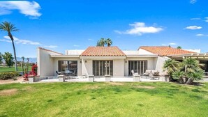 Ein zweistöckiges Haus mit einem Ziegeldach, einer Eingangsterrasse mit Sitzgelegenheiten und einem gepflegten Rasen.