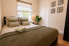 A neatly made bed with a green blanket, a bedside lamp, and a potted plant.