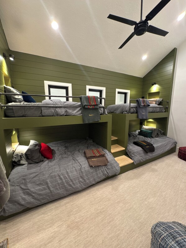 Une chambre avec des lits superposés, un ventilateur de plafond, des murs verts et plusieurs lits.