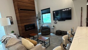 A modern living room with a wooden accent wall, a flat-screen TV, a ceiling fan, and a dining area with a marble countertop.