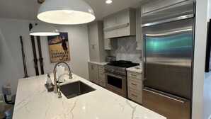 A modern kitchen with a marble countertop, stainless steel appliances, and a pendant light.