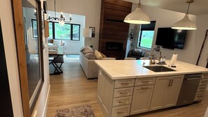 A modern kitchen with a large island, wooden flooring, and pendant lighting.