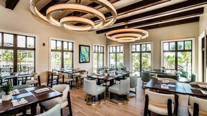 A modern dining area with multiple tables and chairs, large windows with natural light, and a ceiling with circular light fixtures. - Modern Decor With Themed Rooms, With Retro Game Room and Huge Pool in Upscale Resort! #6s820 (Kissimmee)