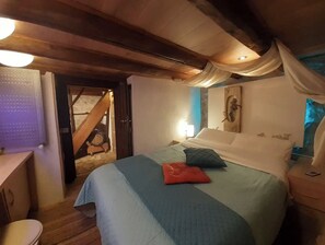 Cozy retreat with a central bed, wooden desk, and staircase leading to an upper level.