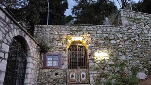 Un edificio de piedra con una entrada central en arco, una ventana pequeña y una reja de metal.