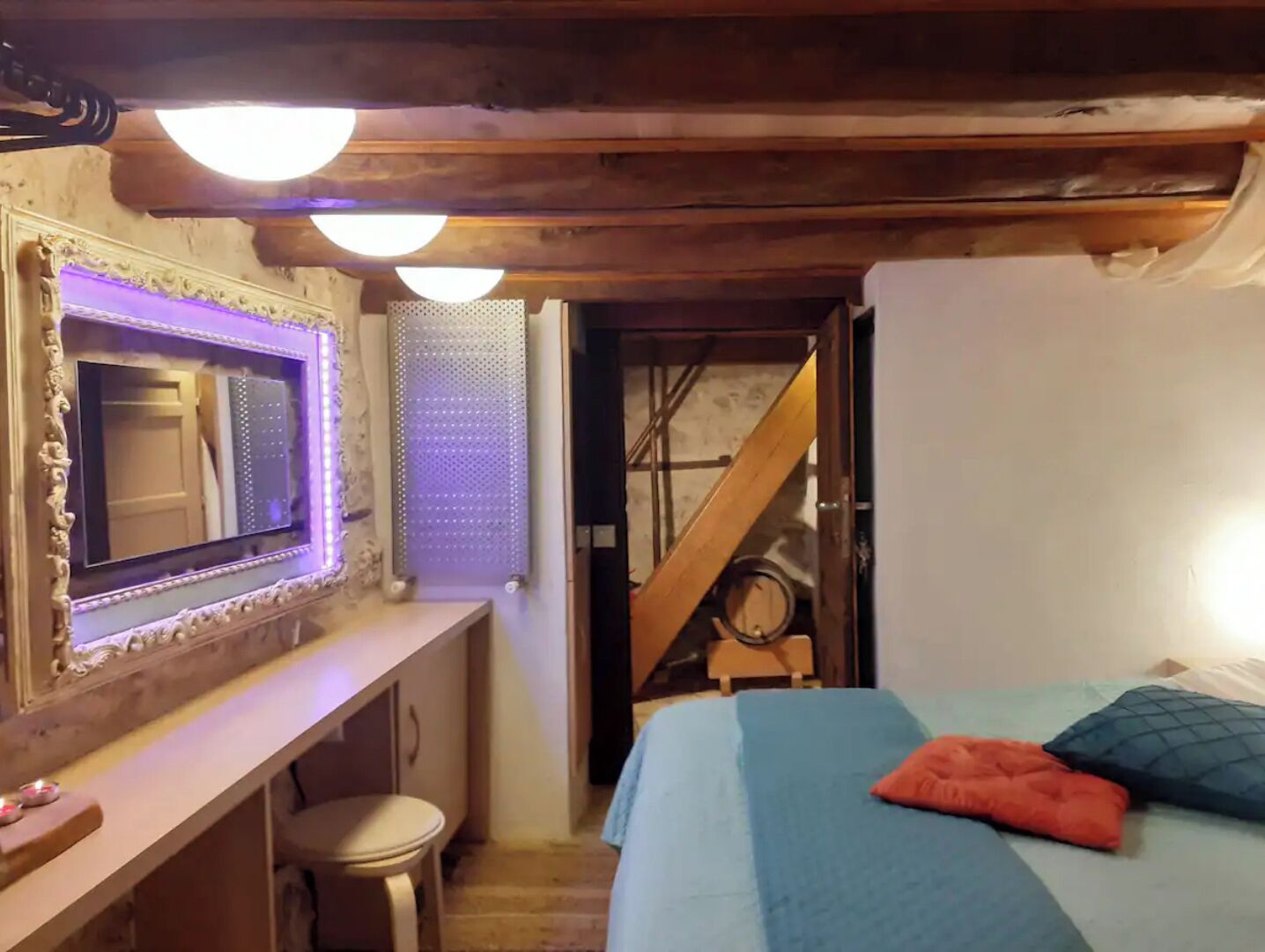 A bedroom with a bed, a mirror, a desk, and a staircase.