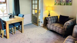 A cozy living room with a plaid sofa, a wooden dining table with chairs, a lamp, and a door with a glass panel. - 2 bedroom accommodation in Cullen (Cullen)