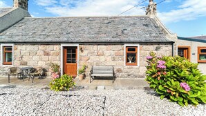 A stone cottage with a wooden door, a bench, and potted plants in front. - 2 bedroom accommodation in Cullen (Cullen)