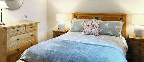 A neatly arranged bedroom with a wooden bed, two bedside tables, a dresser, and a wall-mounted lamp.