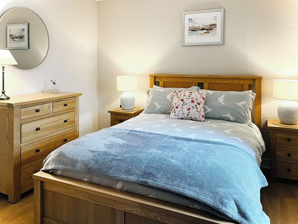 Une chambre à coucher bien rangée, avec un lit en bois, deux tables de chevet, une commode et une lampe fixée au mur.