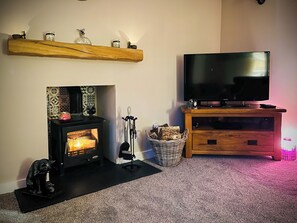 Un salon avec une cheminée, un téléviseur et une étagère en bois ornée d’objets décoratifs.