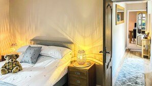 A neatly made bed with a teddy bear, a bedside lamp, and a wooden nightstand with drawers. - 2 bedroom accommodation in Cullen (Cullen)