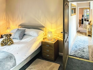A neatly made bed with a teddy bear, a bedside lamp, and a wooden nightstand with drawers. - 2 bedroom accommodation in Cullen (Cullen)