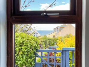 A view through a window with a wooden frame, featuring a garden with various plants and a blue fence. - 2 bedroom accommodation in Cullen (Cullen)
