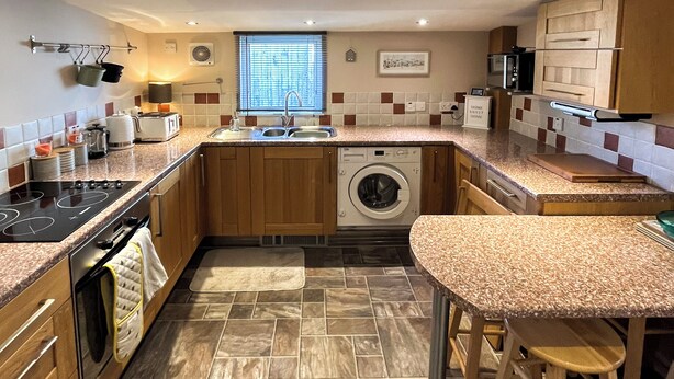 A compact kitchen with a built-in washing machine, a stove, and a sink. - 2 bedroom accommodation in Cullen (Cullen)