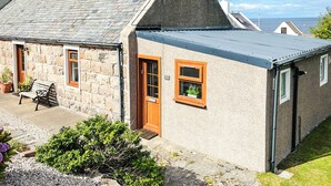 A stone house with a grey roof, a wooden door, and a window with a plant. - 2 bedroom accommodation in Cullen (Cullen)