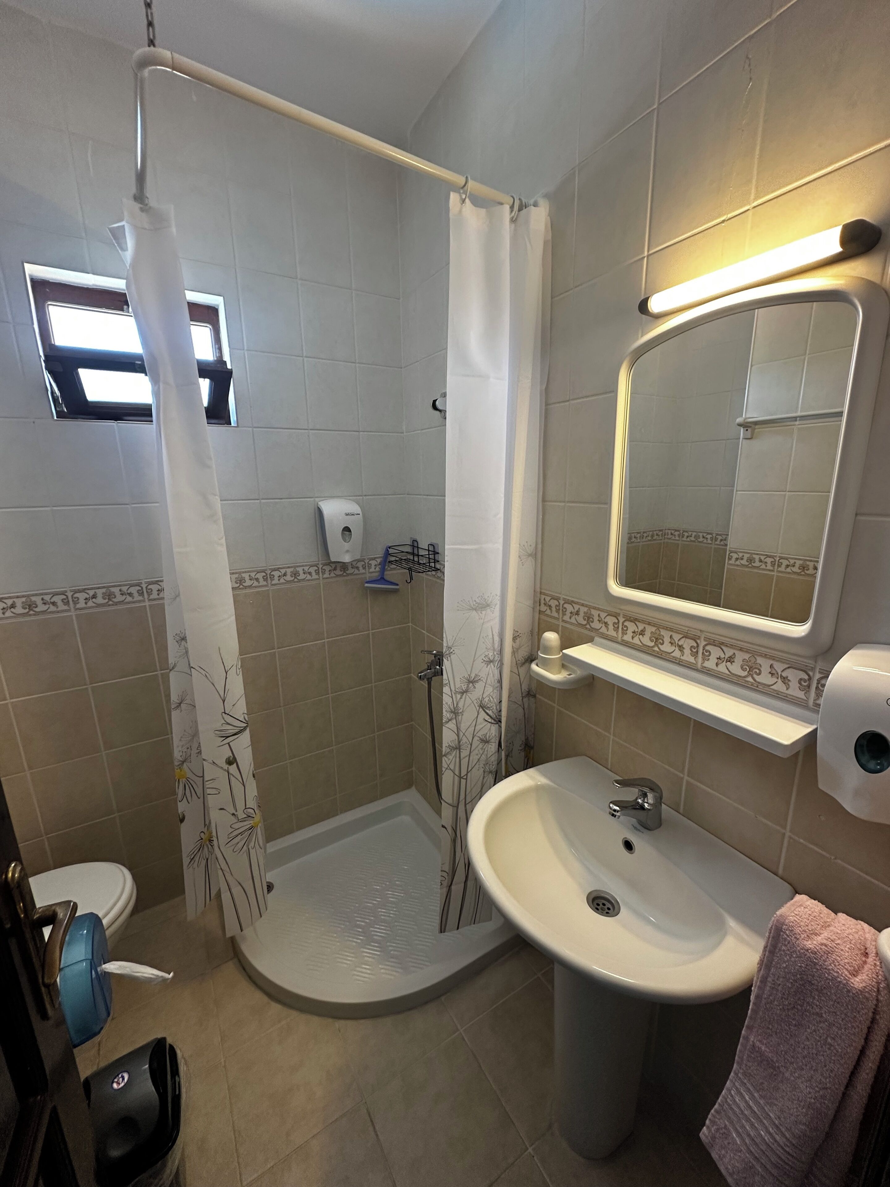A bathroom with a shower, toilet, sink, and a mirror with lights.