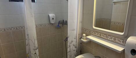 A bathroom with a shower, toilet, sink, and a mirror with lights.
