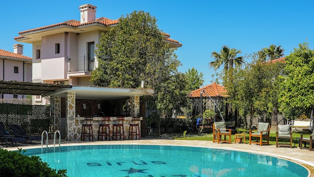 A swimming pool with a bar area, surrounded by outdoor seating and greenery. - Sirius Star (Ortaca)
