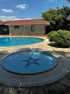 Una piscina con diseño de estrella, rodeada de baldosas de piedra y un edificio de piedra con techo de tejas rojas.