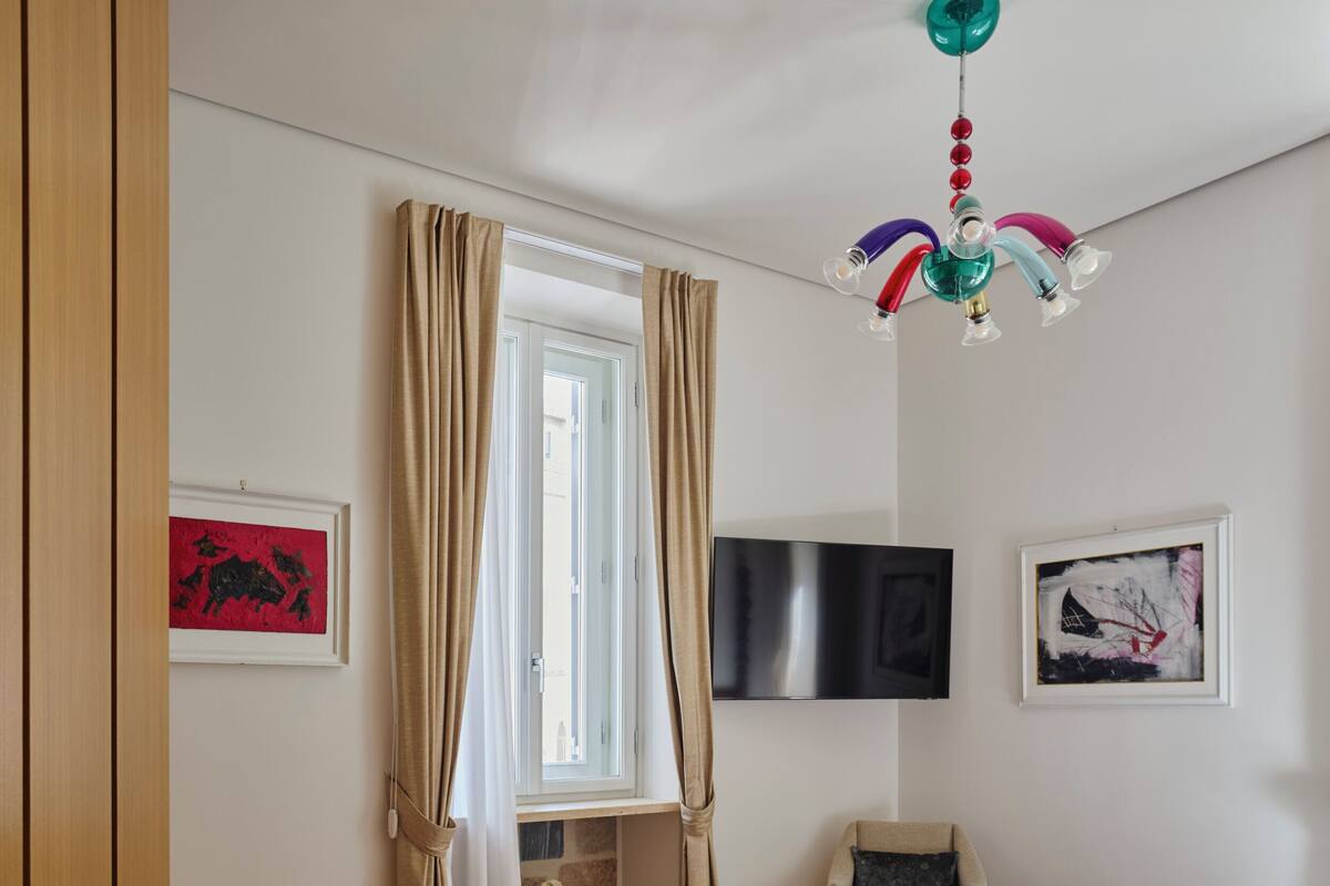 Un dormitorio con una cama, un televisor y una ventana con cortinas.