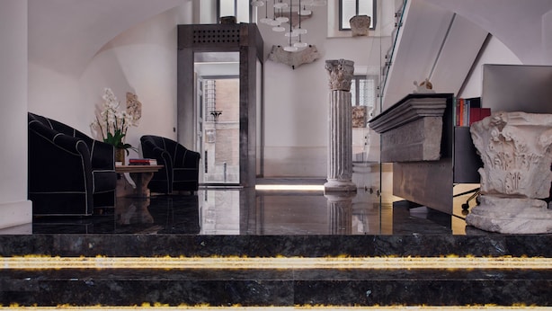 Un hall d’entrée moderne avec des marches en marbre, un canapé noir, une table ornée de fleurs et des colonnes de style classique.