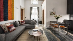 Un salon moderne avec un canapé d’angle gris, une table basse ronde et un coin repas doté de chaises en fil de métal.
